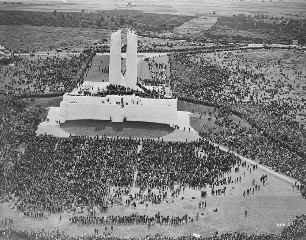 Black and white photograph. Aerial view of the monument and crowd surrounding it. The iconic Mother Canada sculpture is covered by dark cloth.